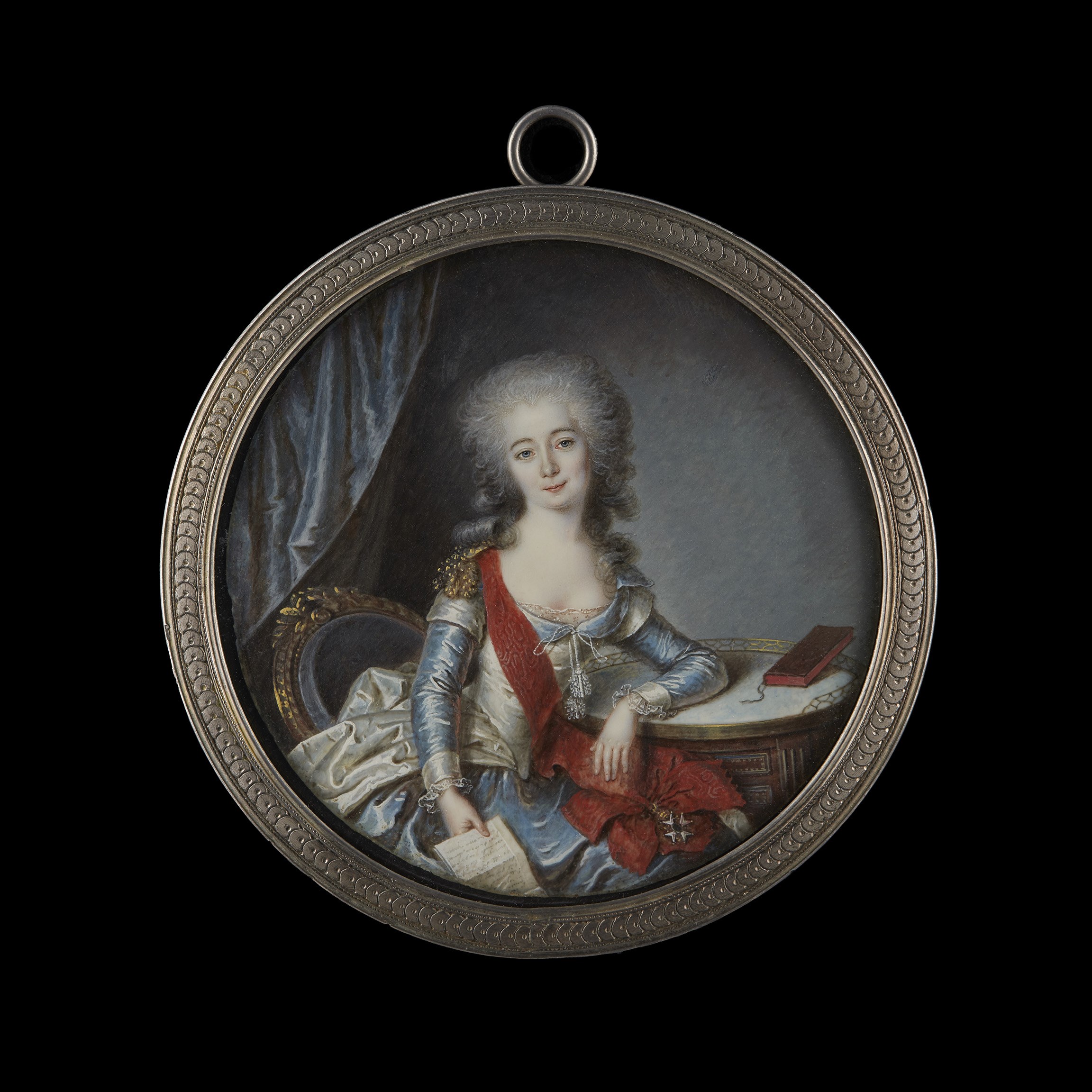 Portrait miniature of a Lady, almost certainly Suzanne Elisabeth de Gaulmyn (1752-after 1804), Countess-Canoness of Saint-Denis Church, Alix (later married name Puy de Semur), wearing white satin dress, a red moiré silk sash, an order and gold epaulette, seated, holding a letter in her right hand and her left arm resting on a table with marble top, maroon covered book beside her; blue silk curtain background